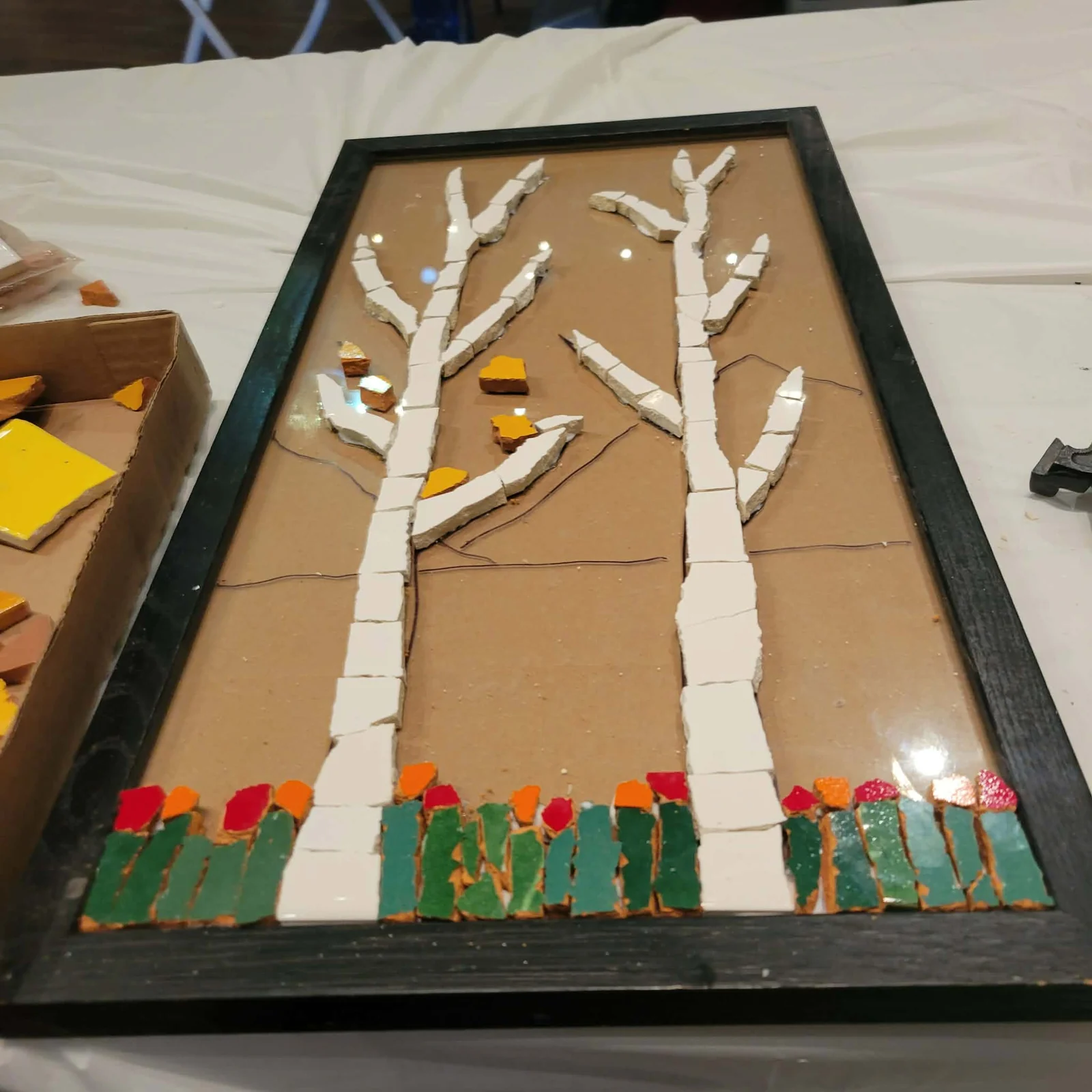 A tree mosaic design with cut ceramic tiles being arranged in a frame.